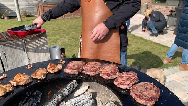 Caucasian man In leather tablier grilling meat on a barbecue outdoor grill. Barbeque autumn time.
