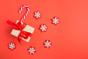 Top view of Christmas gift, caramel cane stick and toy snowflakes  on the red background