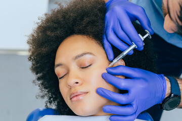 Attractive young African woman is getting a rejuvenating facial injections. She is sitting calmly...