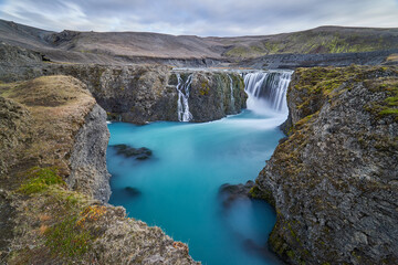 Icelandic waterfalls without tourists, azure blue surface, waters, in the middle of a desolate volcanic desert, rugged landscape with a magical waterfall