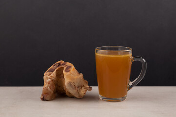 Homemade beef bone broth with natural collagen. Bouillon in a clear mug and a boiled large bone. Selective focus, copy space
