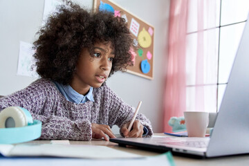 Cute smart african american school pupil kid girl virtual distance learning online watching remote digital class lesson looking at laptop computer tech studying at home writing notes sitting at desk.