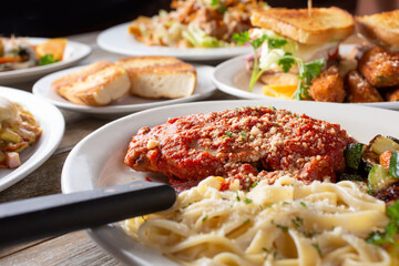 Fototapeta premium A view of a layout of several prepared entrees, featuring a plate of chicken parmigiana and pasta, in a restaurant or kitchen setting.