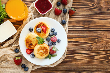 Sweet cheese pancakes with berries and glass of juice on wooden table