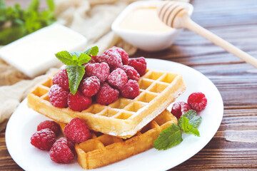 Tasty waffles with fresh raspberries and mint leafs on brown wooden background