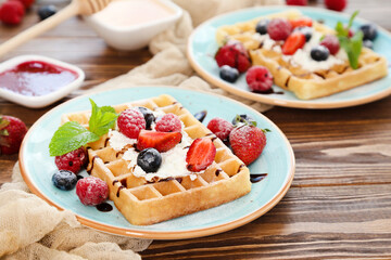 Tasty waffles with fresh berries and whipped cream on brown wooden background