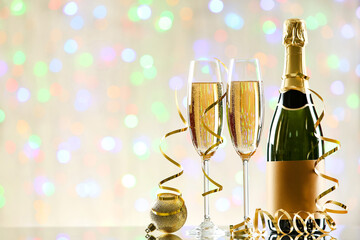 Bottle and glasses of champagne with bauble and ribbons on blurred lights background