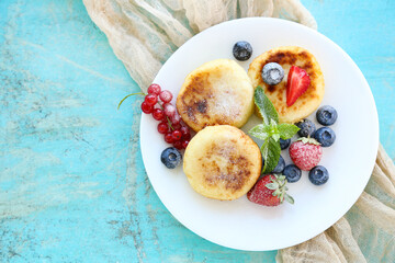 Sweet cheese pancakes with berries and mint leafs on blue background