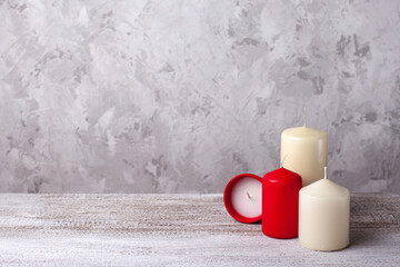two vanilla and two red candles on a wooden table, one red candle in a clay pot on its side on a concrete background, copy space.