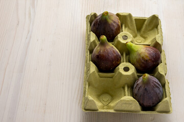 Top view of four figs in yellow egg carton, on white wooden table, in portrait, with copy space