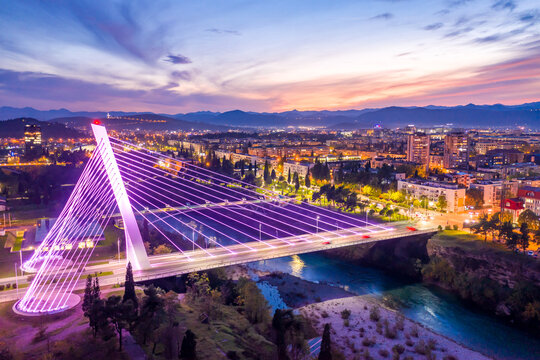 Fototapeta Podgorica, Montenegro, at night, featuring illuminated Millennium bridge in the city center, under colorful sunset sky. Cityscape of the capital of a small country in the Balkans, south east Europe.