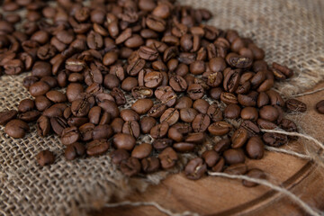 Scattered roasted coffee beans on burlap on a wooden cutting board. Close-up.