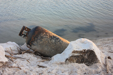 rusty gas cylinder abandoned on the sand of the water shore