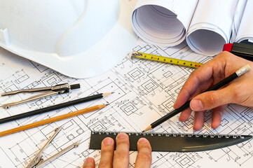 Close up view at human hands drawing with pencil and ruller on blueprints, making a correction