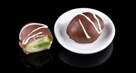 Chocolate truffle with green grape filling isolated on black background. Closeup photography.