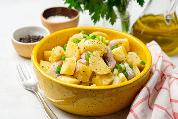 Potato salad with salted herring and onion in ceramic bowl on concrete background