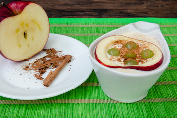 Arroz con leche con manzana, uva y canela, sobre un mantel verde, media manzana y ramitas de canela sobre la mesa
