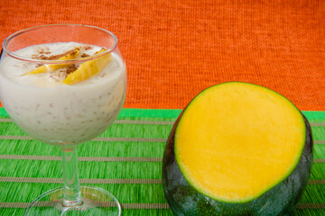 Taza de arroz con leche con mango y canela, sobre un mantel verde, medio mango sobre la mesa