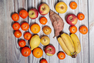 Many orange autumn fruits like mandarins, apples, pears and bananas on a wooden surface