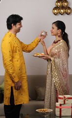 Good looking husband performing Karwa Chauth traditions of offering water to her fasting wife in...