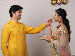 Indian smart couple eating sweet laddu on karva chauth Diwali or anniversary, selective focus....