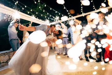 groom and bride kissing among guests with sparklers at the wedding party