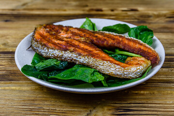 Plate with roasted salmon steak and spinach leaves on a wooden table