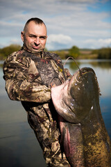 Naklejka premium Fisherman holding a giant catfish. Catch of fish, freshwater fishing, monster fish