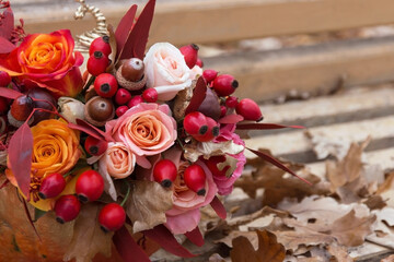 Red pink orange autumn bouquet by florist with rose flowers, fall leaves, rosehip berries and acorn close up, floral background