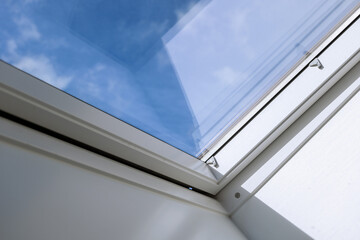 Fototapeta premium Interior view and close-up detail at closed white Tilt Window Skylights at attic and background of sunny blue sky.