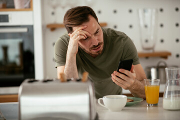 Young man eating breakfast and reading the news online. Handsome man enjoying at home