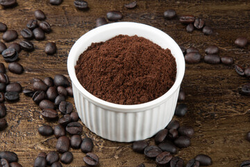 Roasted coffee beans in powder in white bowl. Rustic background.