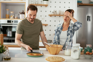 Fototapeta na wymiar Husband and wife making pancakes at home. Loving couple having fun while cooking.