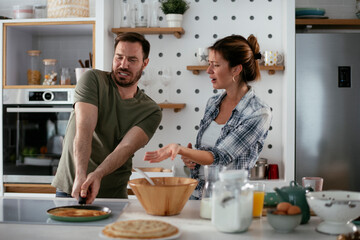 Husband and wife making pancakes at home. Loving couple having fun while cooking.