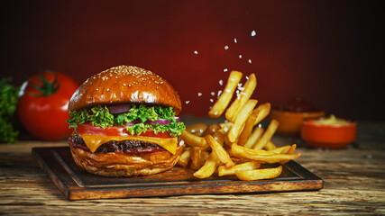 French fries fall next to cheeseburger, lying on vintage wooden cutting board, Freeze motion.