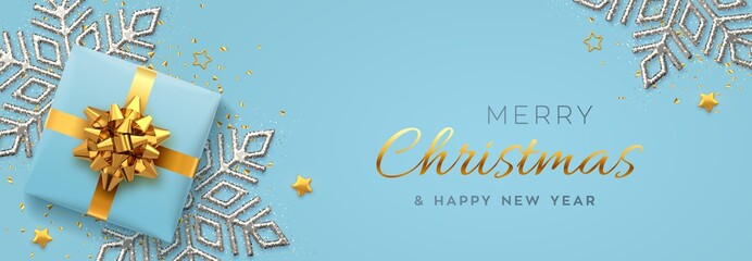Fototapeta na wymiar Christmas banner. Realistic blue gift box with golden bow, silver shining snowflake, gold stars and glitter confetti. Xmas background, horizontal poster, greeting cards, headers website. Vector.
