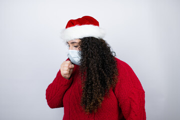 Young beautiful woman wearing a Santa hat over white background with her hand to her mouth because she's coughing with mask with her hand to her mouth because she's coughing with mask