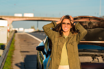 Obraz premium Stressed young woman standing near her broken car on the highway roadside.