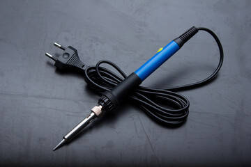 Soldering iron with a blue handle on the old black desktop surface.