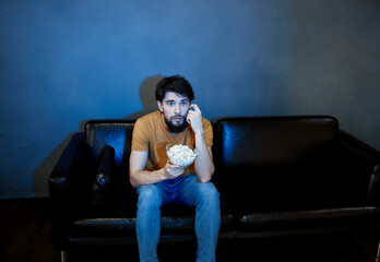 A man sits on a sofa indoors and watches TV front view