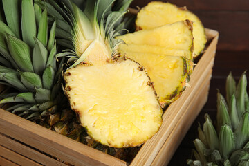Tasty cut pineapples in wooden crate on table, closeup