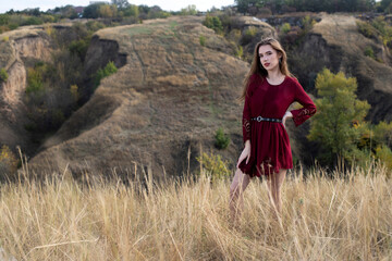 young and beautiful girl model in a red dress posing in nature among the hills