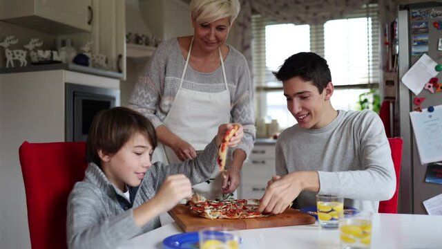 Mother and sons eating pizza for lunch at home
