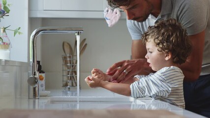 Father helping young son to wash hands in kitchen sink during health pandemic - shot in slow motion - Powered by Adobe