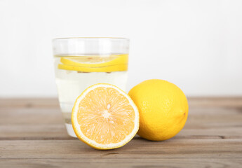 A glass of lemonade and a whole lemon and a half cut lemon next to the glass