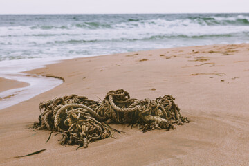 Obraz premium The old rope is lying on the sand on the beach against the background of the sea and waves.