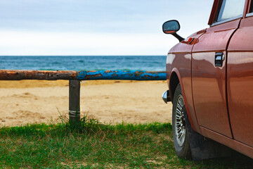 Old brown car on the sandy beach with a blue log fence, summer vacation at the sea.