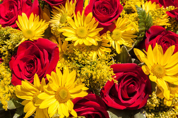 Close up of a cluster of red roses and yellow daisy flowers.