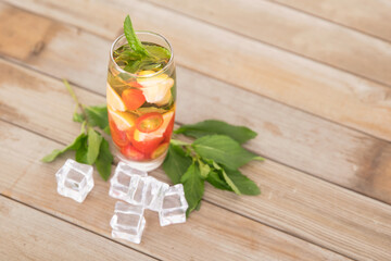 A glass of iced lemon mixed fruit tea with fresh mint leaves and ice cubes scattered on the table
