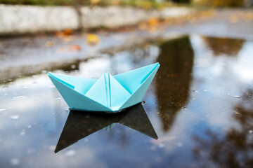 one blue paper ship floating on a water surface. outdoors. autumn season. greeting card with copy space. leadership conceptual. freedom concept